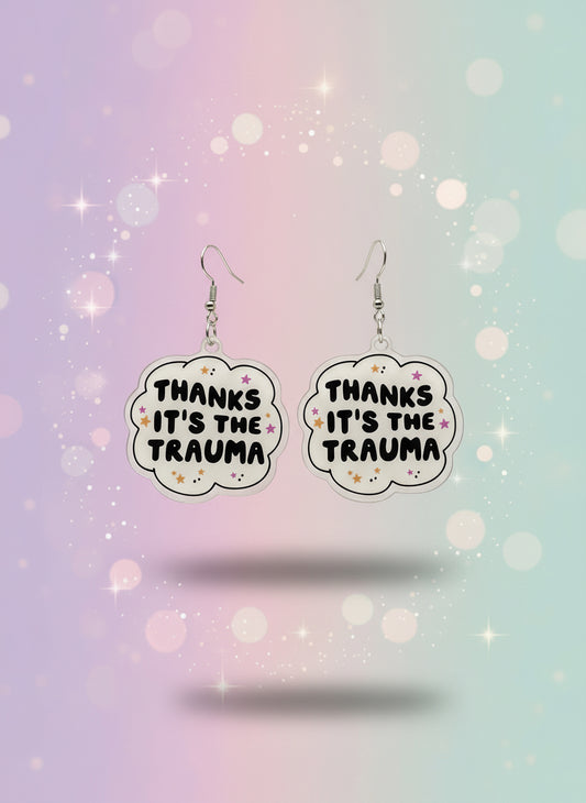 Earrings on a card with text 'THANKS IT'S THE TRAUMA' against a neutral background