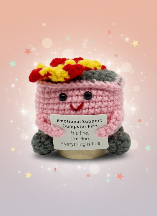 Crocheted character with a sign reading 'Emotional Support Dumpster Fire' on a white background