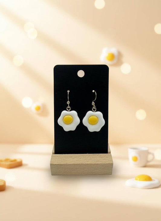 Egg-shaped earrings on a black card with a wooden stand against a white background
