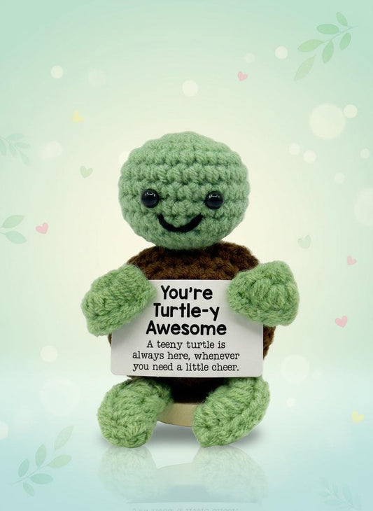 Knitted turtle toy holding a sign saying 'You're Turtle-y Awesome' on a white background