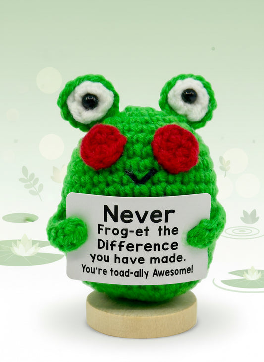 Green crocheted frog with sunglasses holding a sign on a white background