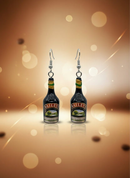Baileys bottle-shaped earrings on a black card with a wooden stand.