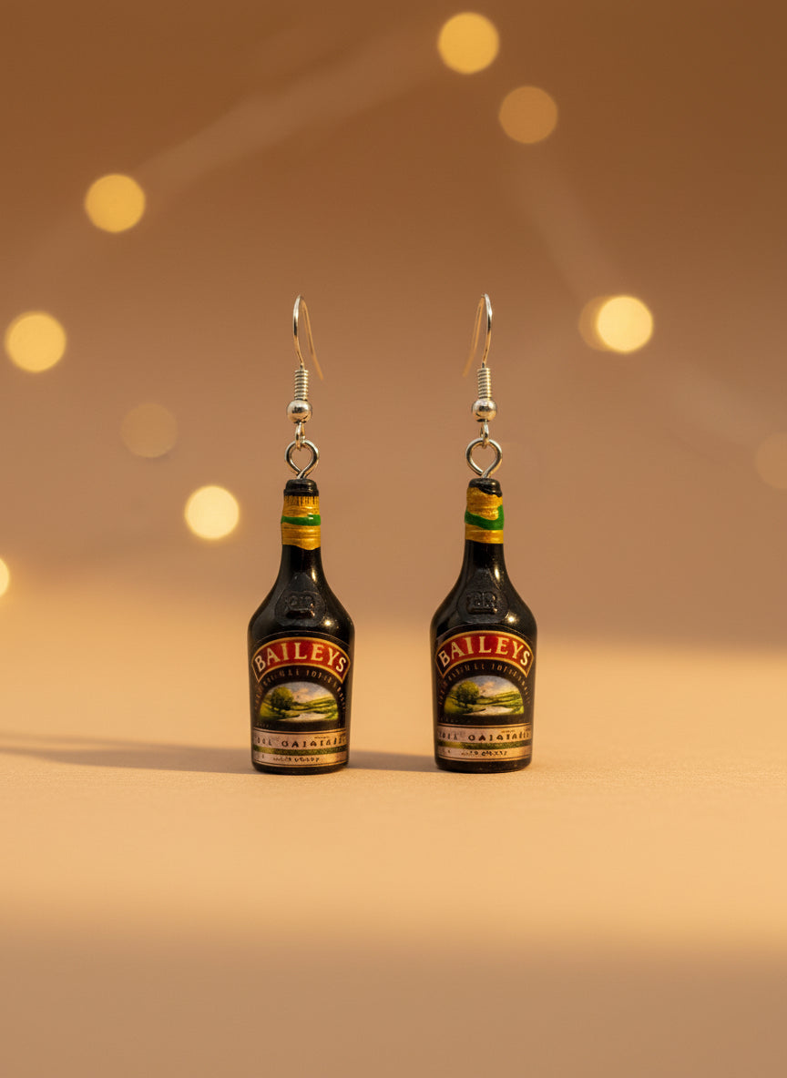 Baileys bottle-shaped earrings on a black card with a wooden stand.