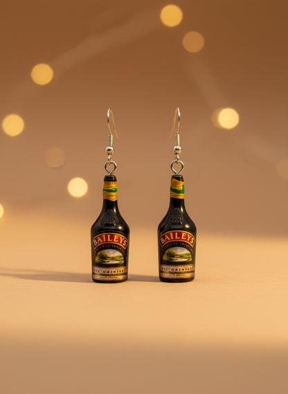 Baileys bottle-shaped earrings on a black card with a wooden stand.