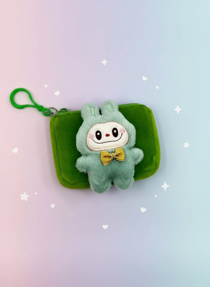 Plush toy in a green outfit with a yellow bow tie on a green pouch against a white background