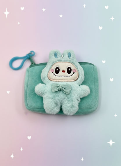 Plush toy with a bow on a small green pouch against a light gray background