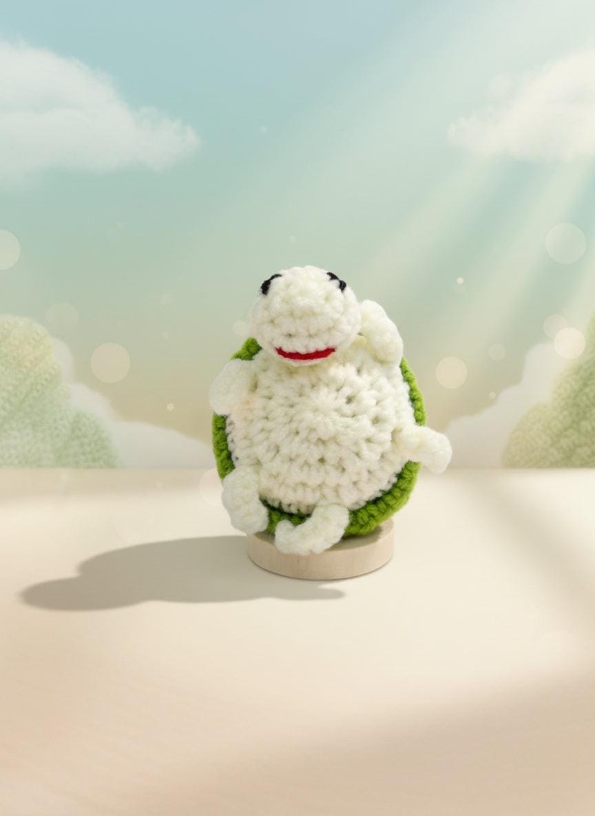 Crochet turtle plushie by Craft-N-Crumble™ sitting on a stand, showcasing its cute design and soft yarn.