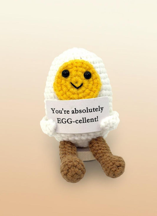 Emotional support egg plushie with a smiley face holding a sign that says 'You're absolutely EGG-cellent!'