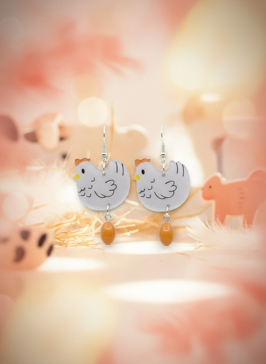 Pair of chicken-shaped earrings on a wooden stand with a white background