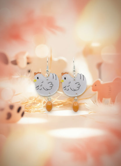 Pair of chicken-shaped earrings on a wooden stand with a white background