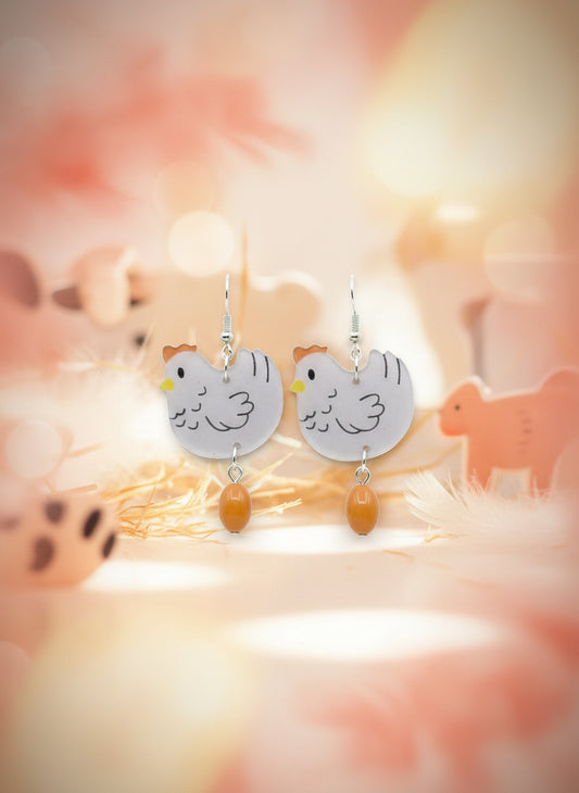 Pair of chicken-shaped earrings on a wooden stand with a white background