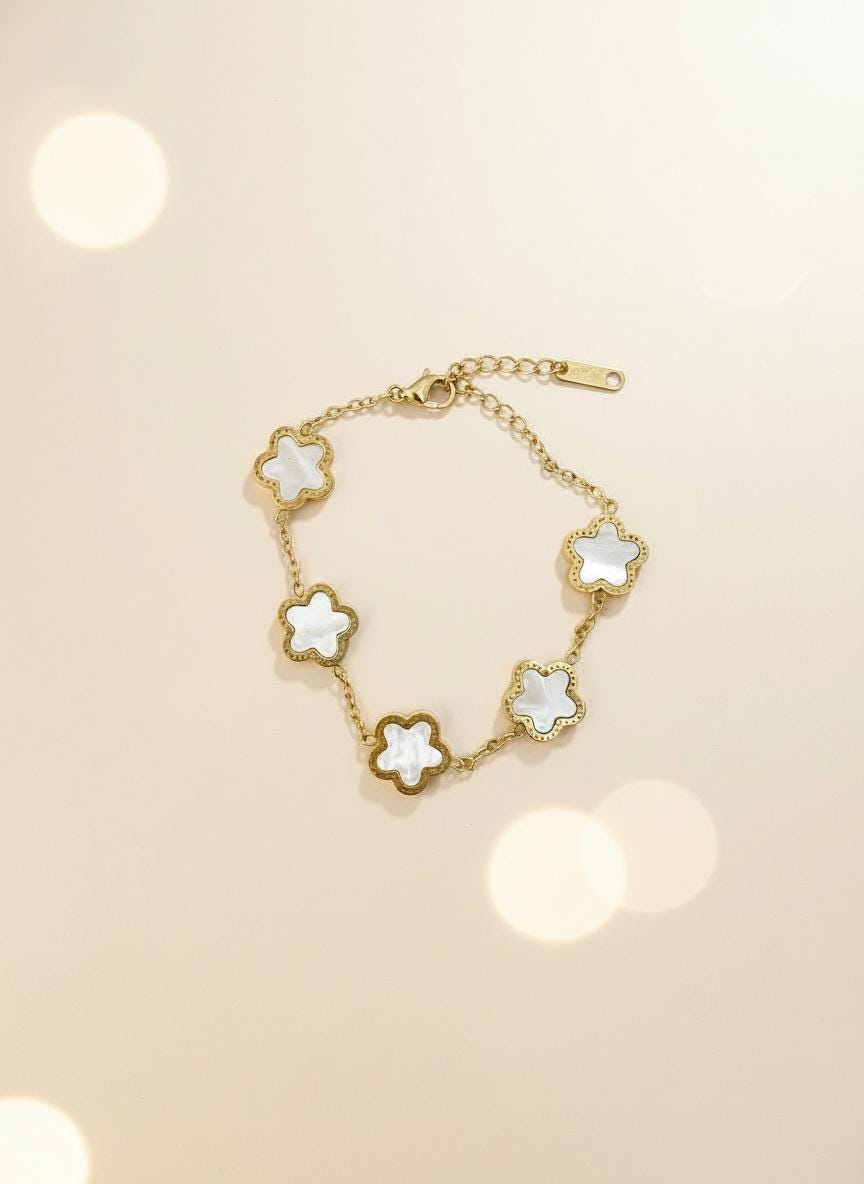 Gold bracelet with white flower-shaped charms on a light gray background