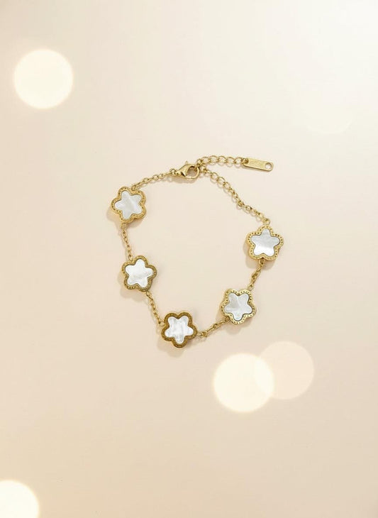 Gold bracelet with white flower-shaped charms on a light gray background