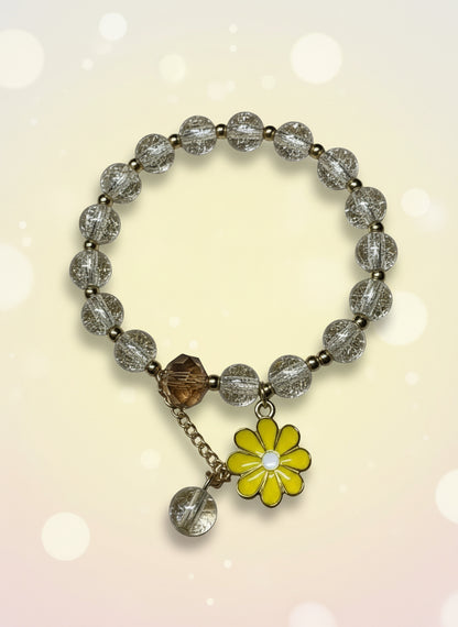 Bracelet with clear beads and a yellow flower charm on a beige background