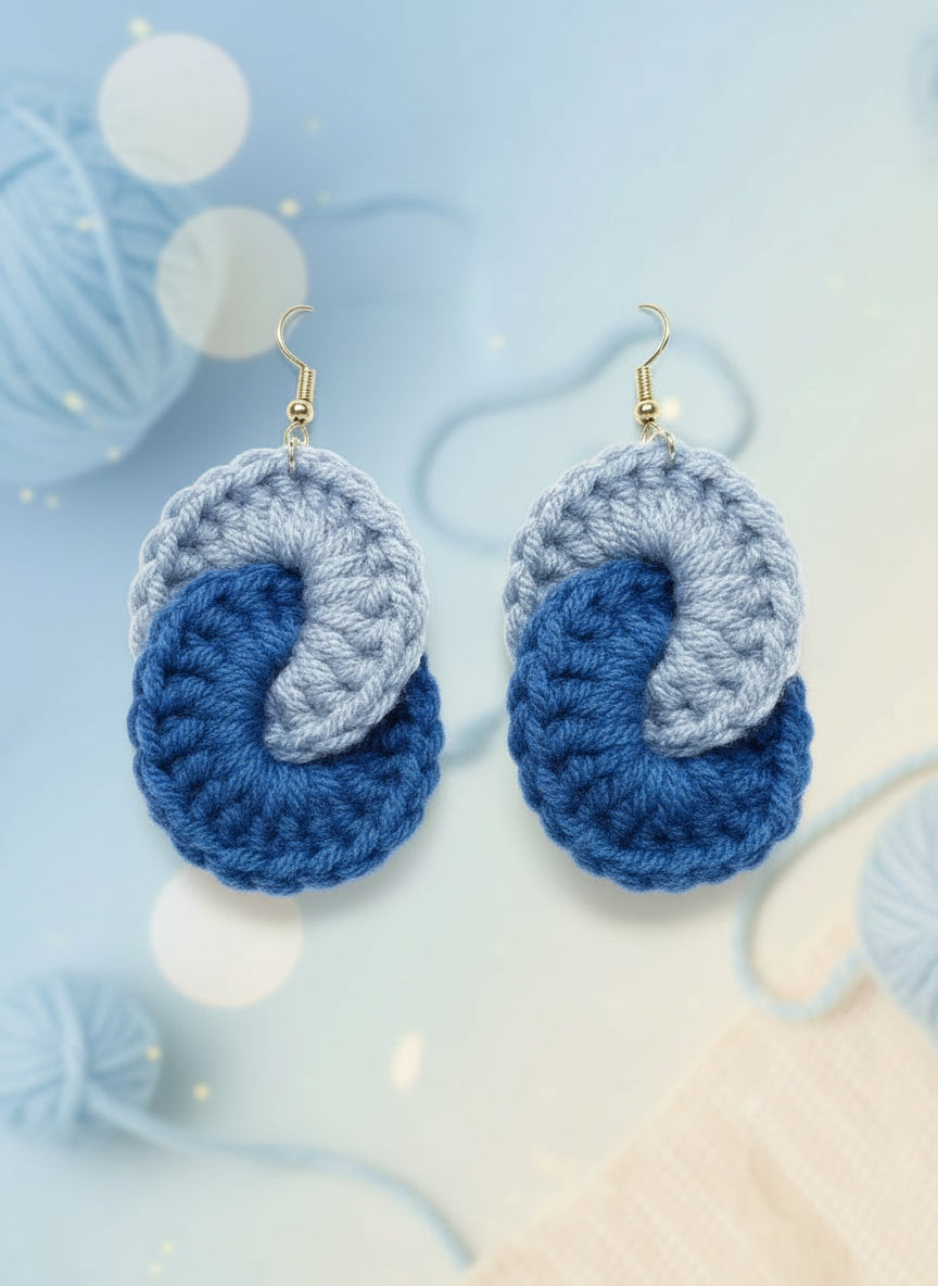 Pair of blue and gray crocheted earrings on a reflective surface.