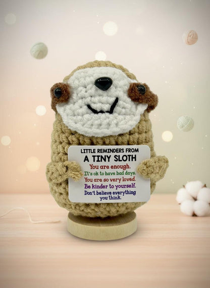 Crocheted sloth toy holding a sign with motivational message on a white background