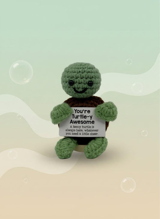 Crocheted turtle plush toy with a message tag on a white background