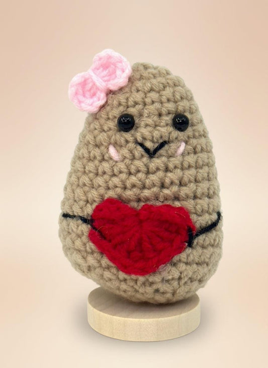 Adorable emotional support potato plushie holding a red heart, handmade from soft yarn with a pink bow on its head.