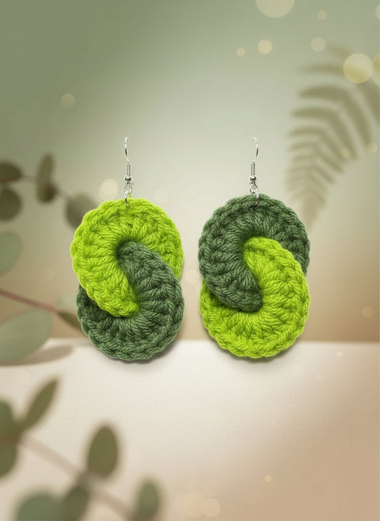 Two green knitted earrings on a reflective surface