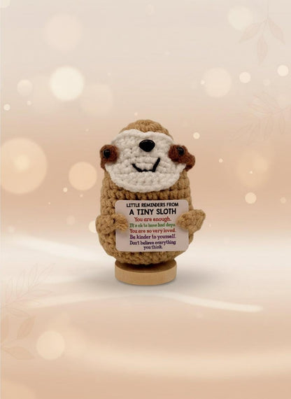 Crocheted sloth toy with a message card on a white background