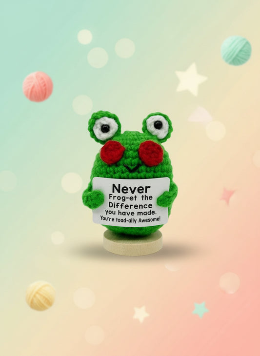 Crocheted frog toy holding a sign with text on a white background