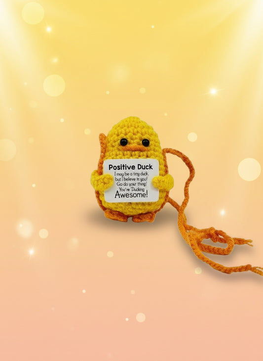 Crocheted Positive Duck toy with a tag on a white background